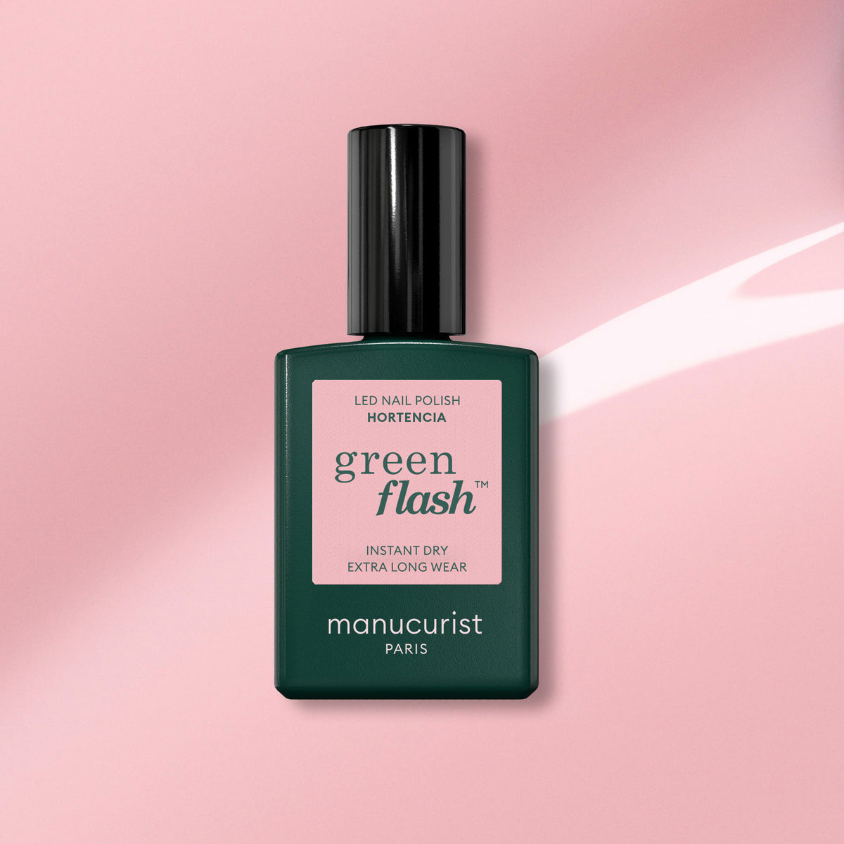 Un flacon de vernis gel Manucurist dans la teinte Hortencia repose sur un fond rose, avec l’étiquette « Séchage instantané, tenue extra longue ».