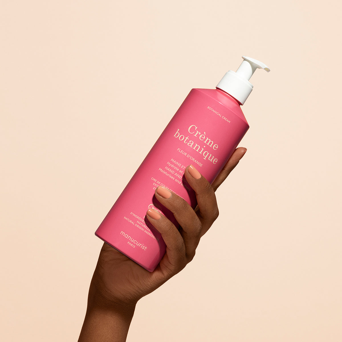 Une main tient un flacon rose de Crème Mains &amp; Corps Apaisante Fleur d&
