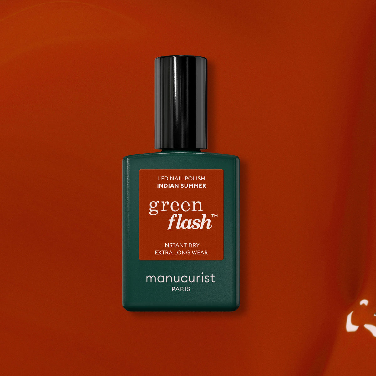 Un flacon de vernis à ongles LED Manucurist Indian Summer Green Flash — une teinte rouge ocre — se détache sur un fond orange-rouge assorti, avec un flacon vert foncé, un capuchon noir et un texte blanc.