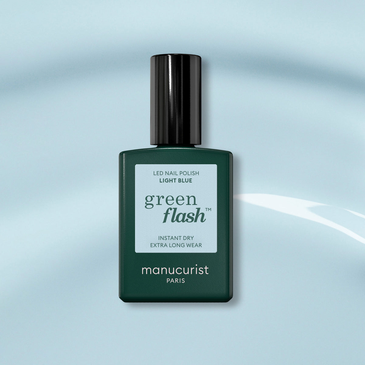 Un flacon de vernis gel Manucurist Light Blue Green Flash, avec un bouchon vert foncé, est posé sur un fond bleu doux. L’étiquette met en avant un séchage instantané et une tenue extra-longue pour cette teinte bleu ciel pastel.