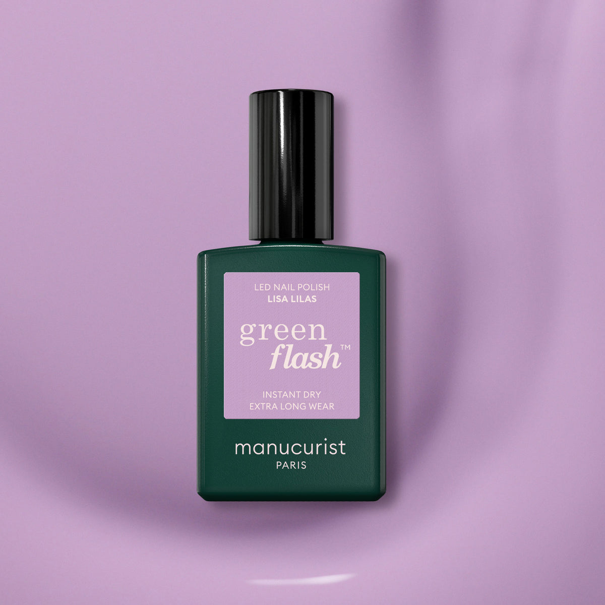 Un flacon de vernis gel Manucurist Lisa Lilas avec une base vert foncé, un bouchon noir et une étiquette violette repose sur une surface lisse de couleur mauve clair, dégageant une subtile ambiance années 90.