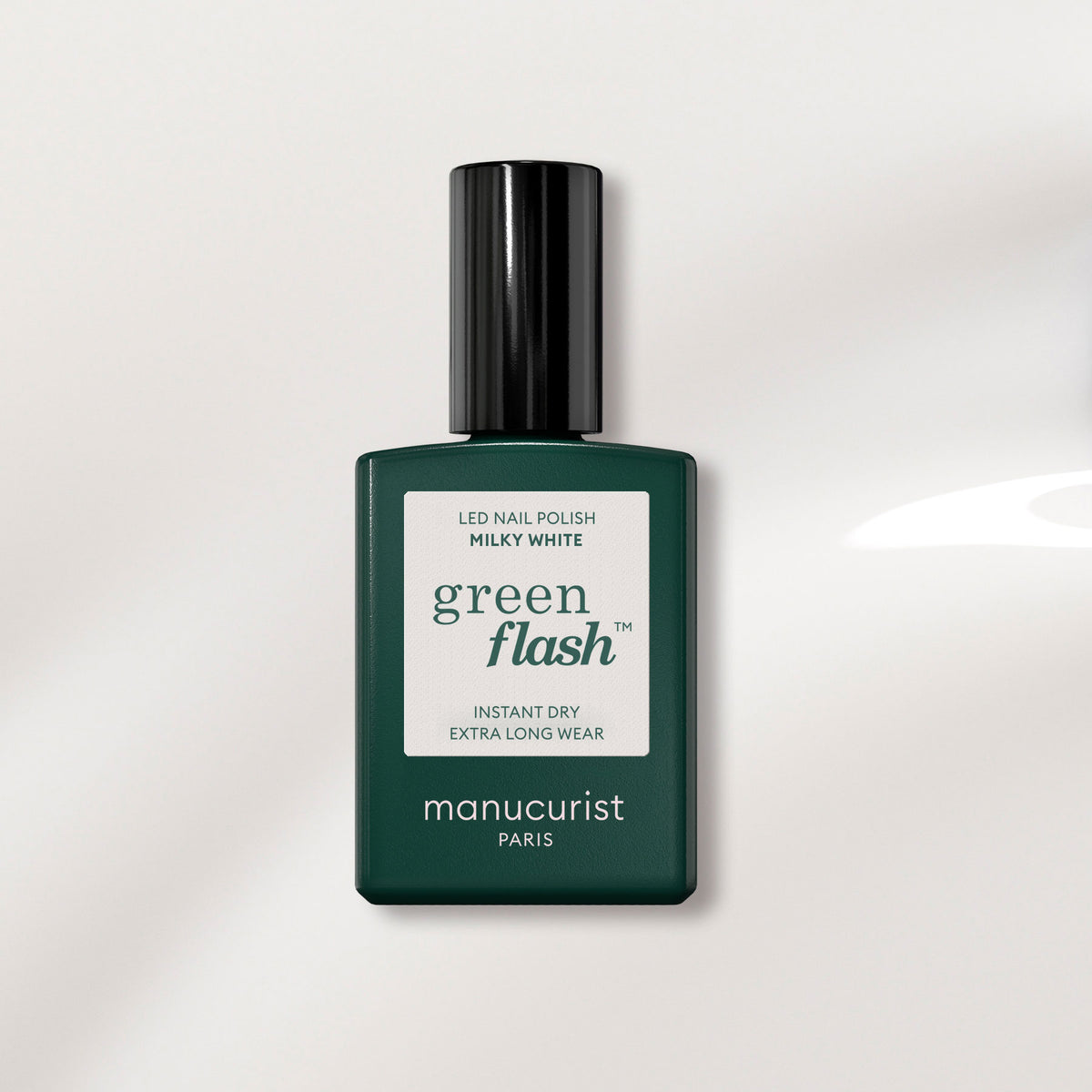 Un flacon de vernis gel Milky White de Manucurist, avec une base rectangulaire vert foncé et un capuchon noir, présenté sur un fond clair.