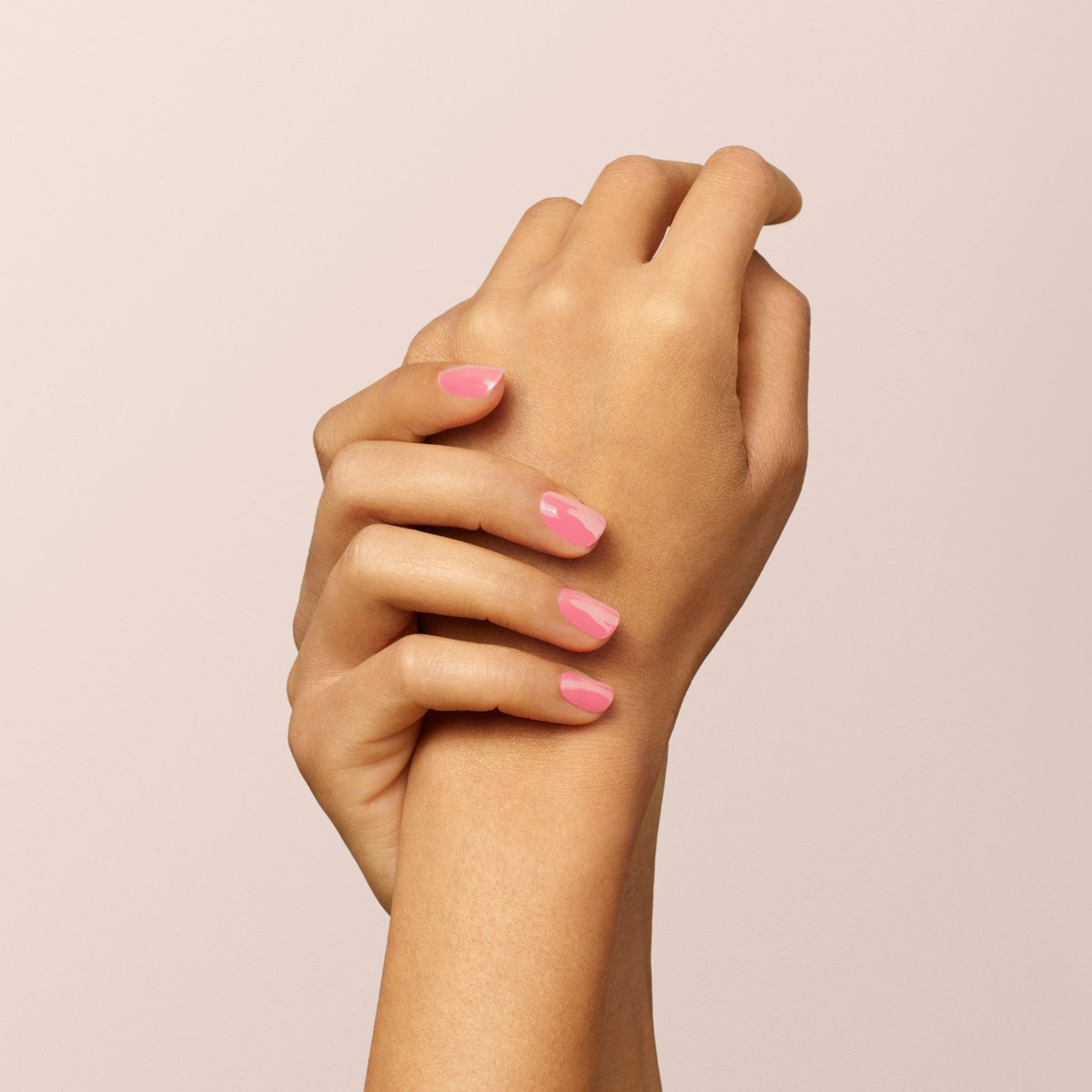 Two hands with light brown skin are clasped together against a pale pink background, nails neatly manicured and painted with Manucurist&