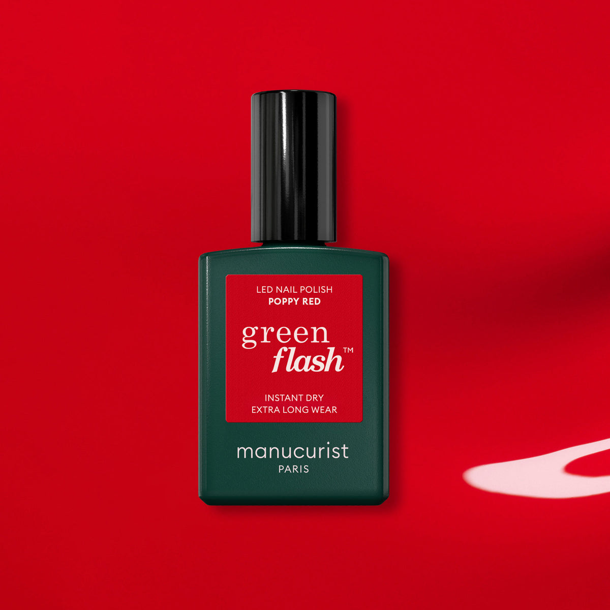 Un flacon de vernis gel Poppy Red Manucurist avec un bouchon noir repose sur un fond rouge intense et projette une ombre spectaculaire.