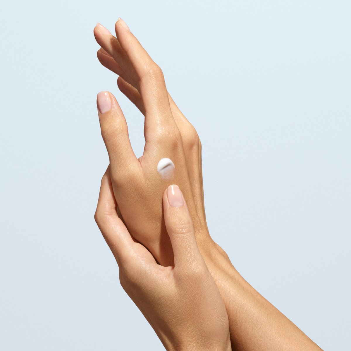 Gros plan sur deux mains aux ongles naturels ; l’une applique une petite quantité de crème pour les mains Everyday Lavender de Manucurist - Cosmos Organic sur le dos de l’autre, sur un fond bleu clair.